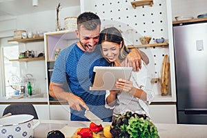 Happy couple is enjoying and preparing healthy meal in their kitchen and reading recipes on the digital tablet