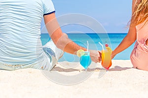 Happy couple enjoying tropical cocktails on sand beach