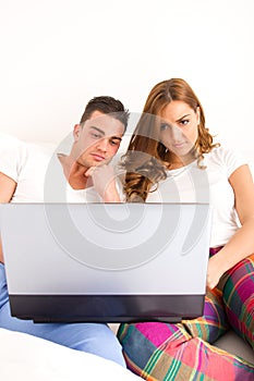Happy couple enjoying using laptop computer in bed
