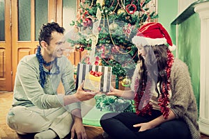 Happy couple exchanging gifts at home by Christmas tree