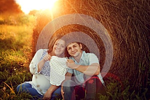 Happy couple expecting a baby sitting on the field near the hays