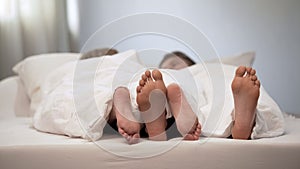 Happy couple feet in honeymoon bed, lovely conversation in morning, marriage