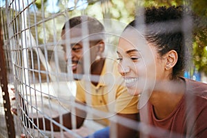 Happy couple, fence and smile at animal shelter, pet centre or zoo looking for a cute companion to adopt. Black man and