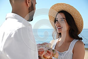 Happy couple with flowers at beach near sea. Honeymoon trip