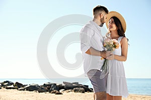 Happy couple with flowers on beach near sea. Honeymoon trip