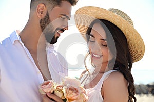 Happy couple with flowers at beach near sea. Honeymoon trip