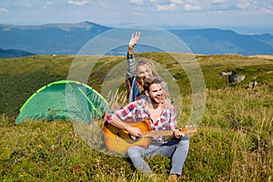 Happy couple friends camping, and playing guitar together in summer at nature forest. Couple in love on camp.