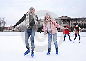 Happy couple with friends skating along ice rink outdoors
