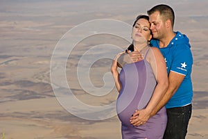 Happy Couple, Future Parents, Kissing Near The crater At Sunset. Man Hugging His Pregnant Woman