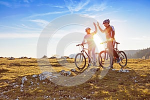 Happy couple goes on a mountain asphalt road in the woods on bikes with helmets giving each other a high five