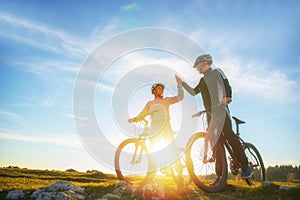 Happy couple goes on a mountain road in the woods on bikes with helmets giving each other a high five