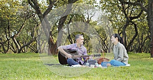 Happy couple with guitar having rest on picnic in the park on the lawn. Romance, vacation and summer concept