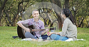 Happy couple with guitar having rest on picnic in the park on the lawn. Romance, vacation and summer concept