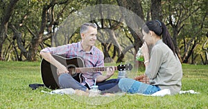 Happy couple with guitar having rest on picnic in the park on the lawn. Romance, vacation and summer concept.