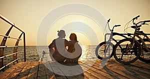 A happy couple, a guy in a light shirt and a girl in a straw hat, look at each other and sit on a beach covered with