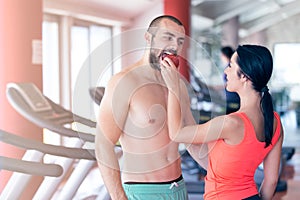 Happy couple in gym feeding each other with apple