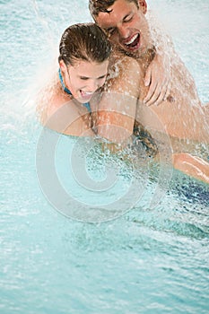 Happy couple have fun under water stream in pool