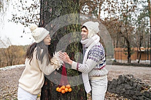 Happy couple have a fun in winter forest. Tangerine mood in winter holidays. Emotional young couple in white sweater having fun