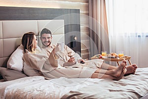 Happy couple having breakfast in luxury hotel room, watching TV