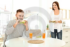 Happy couple having breakfast with sandwiches at table