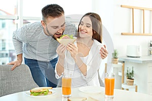 Happy couple having breakfast with sandwiches at table