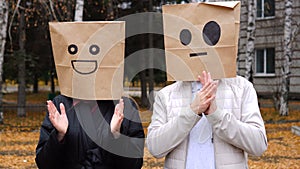 Happy couple having fun by cover head with paper bags doing congratulatory gestures applauding