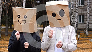 Happy couple having fun by cover head with paper bags doing funny dance outdoors