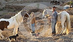 Happy couple having fun with horses inside stable - Young farmers sharing time with animals in corral ranch