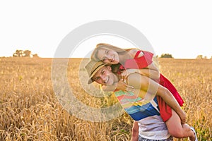 Happy Couple Having Fun Outdoors on wheat field over sunset. Laughing Joyful Family together. Freedom Concept. Piggyback