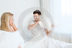 Happy couple having pillow fight in bed at home