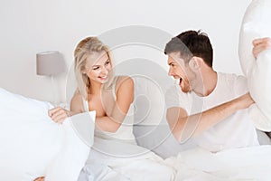 Happy couple having pillow fight in bed at home