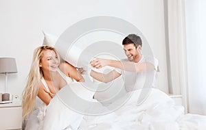 Happy couple having pillow fight in bed at home