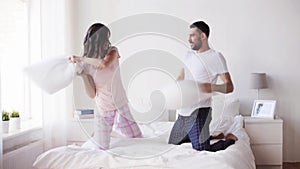 Happy couple having pillow fight in bed at home