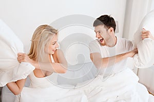 Happy couple having pillow fight in bed at home