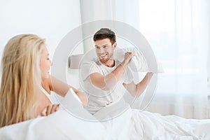 Happy couple having pillow fight in bed at home