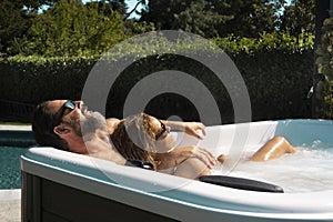 Happy couple having relax inside the hydromassage pool in the garden at home. Luxury lifestyle people. Man and woman sunbathing