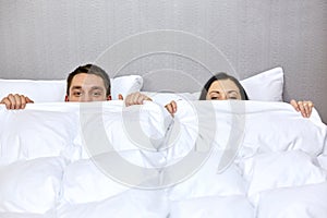 Happy couple hiding under blanket in bed