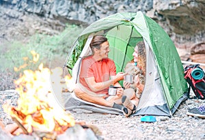 Happy couple of hikers with their dog camping with tent around rock mountains next to fire