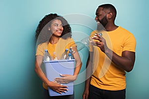 Happy couple hold a plastic container with bottles over a light blue color. Concept of ecology, conservation, recycling