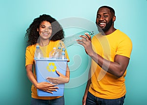 Happy couple hold a plastic container with bottles over a light blue color. Concept of ecology, conservation, recycling