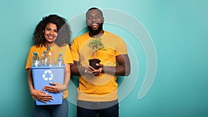 Happy couple hold a plastic container and a small tree over a light blue color. Concept of forestation, ecology