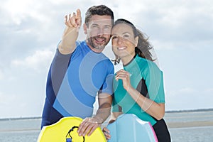 happy couple holding bodyboard pointing