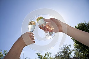 Happy couple holding champagne glasses and raising them against a clear blue summer sky