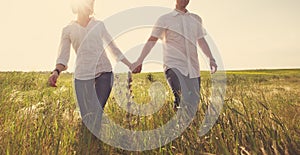 Happy couple holding hands walking through a meadow