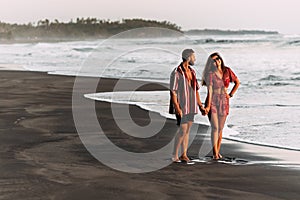 Happy couple holding hands walking on the sandy beach. Couple in love at sunset by the sea. Couple in love on vacation. Honeymoon