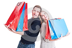 Happy couple holding heavy shopping bags and acting amazed