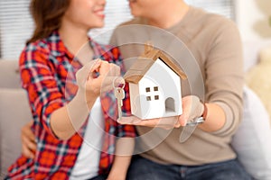 Happy couple holding keys to new home and house miniature - real