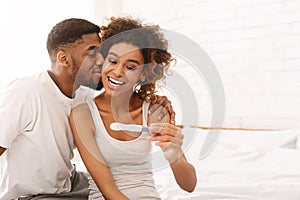 Happy couple holding positive pregnancy test on bed