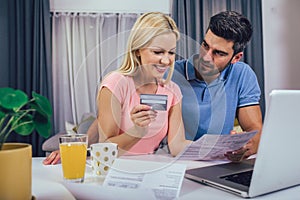 Couple at home paying bills with laptop and credit card