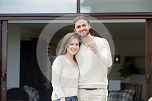 Happy couple homeowners holding keys standing against new own ho